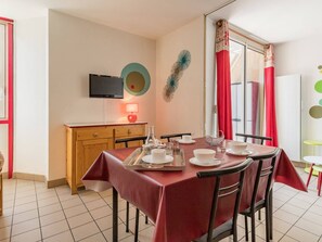 A dining area with a red tablecloth, chairs, a wooden cabinet, a television, and a window with red curtains. - Cozy 2-Room Apartment for 4-6, Near Prorel Cable Car, South-Facing Balcony, Ski Locker (Briançon)