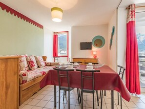 A cozy room with a wooden sofa, a dining table with chairs, and a TV mounted on the wall. - Cozy 2-Room Apartment for 4-6, Near Prorel Cable Car, South-Facing Balcony, Ski Locker (Briançon)