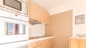 A kitchen with a built-in oven, microwave, and stove, wooden cabinets, and a tiled backsplash. - Cozy 2-Room Apartment for 4-6, Near Prorel Cable Car, South-Facing Balcony, Ski Locker (Briançon)