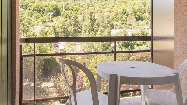 A balcony with a white table and two white chairs, overlooking a forested hillside. - 2-Room Apartment - Sleeps 6, Near Prorel Lift and Briançon Center (Briançon)