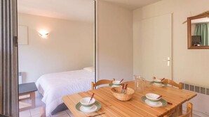 A hotel room with a wooden dining table set with bowls and spoons, a bed with white linens, and a sliding door leading to another room. - 2-Room Apartment - Sleeps 6, Near Prorel Lift and Briançon Center (Briançon)
