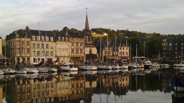 A harbor with boats docked, buildings with historical architecture, and a church spire.