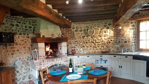 A rustic kitchen with a brick fireplace, white cabinets, and a dining table set for four.