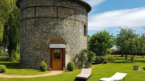 A stone tower with a conical roof, a wooden door, and two sun loungers on a well-maintained lawn.