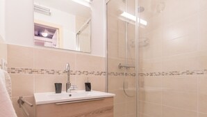 Un baño moderno con cabina de ducha de vidrio, lavamanos blanco sobre un mueble de madera y salpicadero de azulejos.