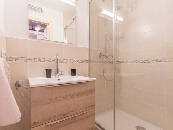A modern bathroom with a glass shower enclosure, a white sink with a wooden vanity, and a tiled backsplash.
