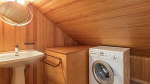 Una habitación pequeña con paneles de madera, un lavabo, una lavadora y un espejo.
