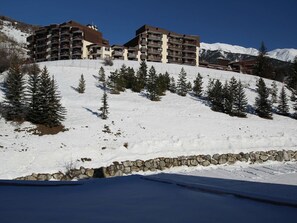 Et hotel med flere etager og balkoner, omgivet af sneklædte skråninger og fyrretræer.