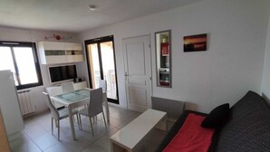 Une cuisine de taille modeste avec des meubles blancs, une table à manger avec des chaises, un canapé agrémenté d’un coussin rouge et un tableau accroché au mur.