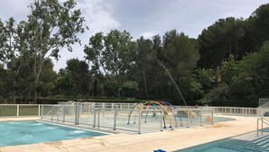Une piscine à l’eau claire, entourée d’une clôture blanche et bordée d’arbres au loin.