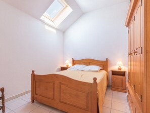 Quarto com cama de madeira, duas mesas de cabeceira com luminárias, um guarda-roupa e um claraboia.