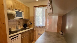 A compact kitchen with wooden cabinets, a microwave, a sink, and a window with lace curtains. - Duplex for 6 in Serre-Chevalier - Chantemerle (Saint-Chaffrey)