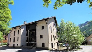 A two-story building with a sloped roof, multiple windows, and a visible staircase leading to an upper floor. - Spacious Triplex 4 rooms, sleeps 7, near slopes, parking, quiet (Le Monêtier-les-Bains)
