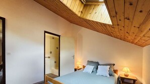 A bedroom with a wooden ceiling, a bed with pillows, a nightstand with a lamp, and a door leading to a bathroom. - Spacious Triplex 4 rooms, sleeps 7, near slopes, parking, quiet (Le Monêtier-les-Bains)