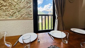 A dining table with plates, cutlery, and glasses, set against a textured wall with a window overlooking a mountainous landscape. - Spacious Triplex 4 rooms, sleeps 7, near slopes, parking, quiet (Le Monêtier-les-Bains)