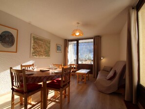 Uma sala de jantar com móveis de madeira, uma mesa coberta por um tecido vermelho e vista para árvores cobertas de neve através de grandes janelas.