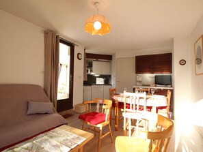 Um espaço compacto com sofá, mesa de jantar, cadeiras, cozinha e televisão.