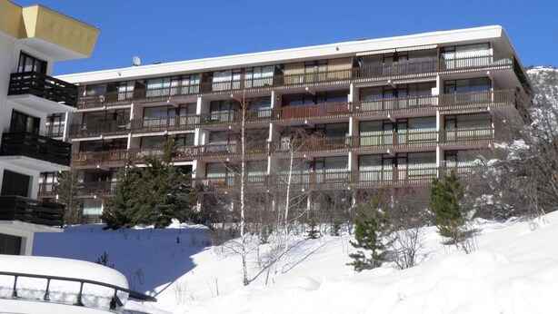 A multi-story hotel with balconies, located in a snowy area with trees.