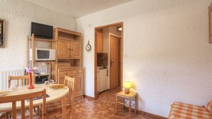 A compact kitchen with wooden cabinets, a microwave, and a dining area with a table and chairs.