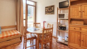 A cozy room with a wooden dining table, chairs, a bench, a television, and a shelf with kitchen appliances.