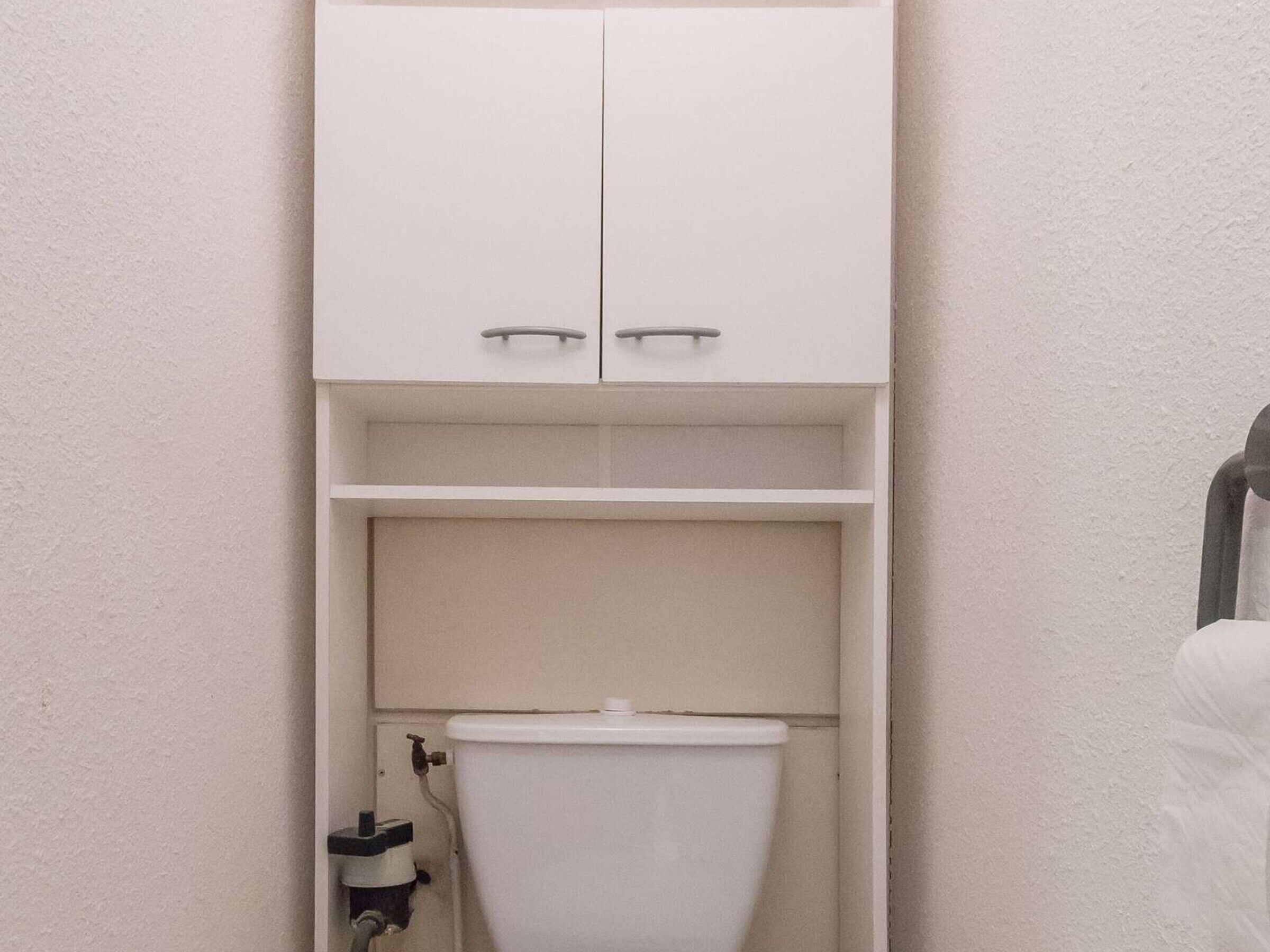Une petite salle de bain compacte, avec des toilettes, un meuble au-dessus et une étagère en dessous.