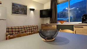 Habitació acollidora amb un sofà escocès, una taula de menjador amb un centre de taula d'un bol trenat, un televisor de pantalla plana i una finestra amb vista a una muntanya i un pont.