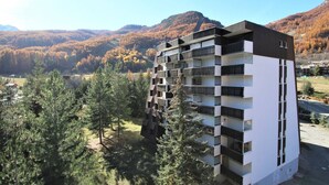 A multi-story building with balconies, surrounded by trees and a mountainous landscape. - Charming Studio for 4 in Serre Chevalier, Close to Slopes & Shops (La Salle-les-Alpes)