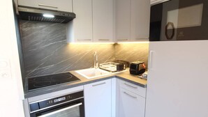 A modern kitchen with a black stovetop, a built-in oven, a microwave, and a toaster. - Charming Studio for 4 in Serre Chevalier, Close to Slopes & Shops (La Salle-les-Alpes)