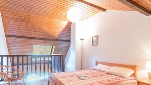 A bedroom with a wooden bed, a chair, a nightstand, and a floor lamp. - Duplex Mezzanine, 6 pers, Serre-Chevalier Chantemerle - Parking, Ski Locker, No Pets (Saint-Chaffrey)