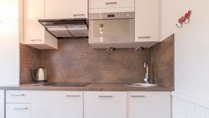 A modern kitchen with white cabinets, a stainless steel range hood, a built-in oven, a sink, and a kettle on the countertop. - Duplex Mezzanine, 6 pers, Serre-Chevalier Chantemerle - Parking, Ski Locker, No Pets (Saint-Chaffrey)