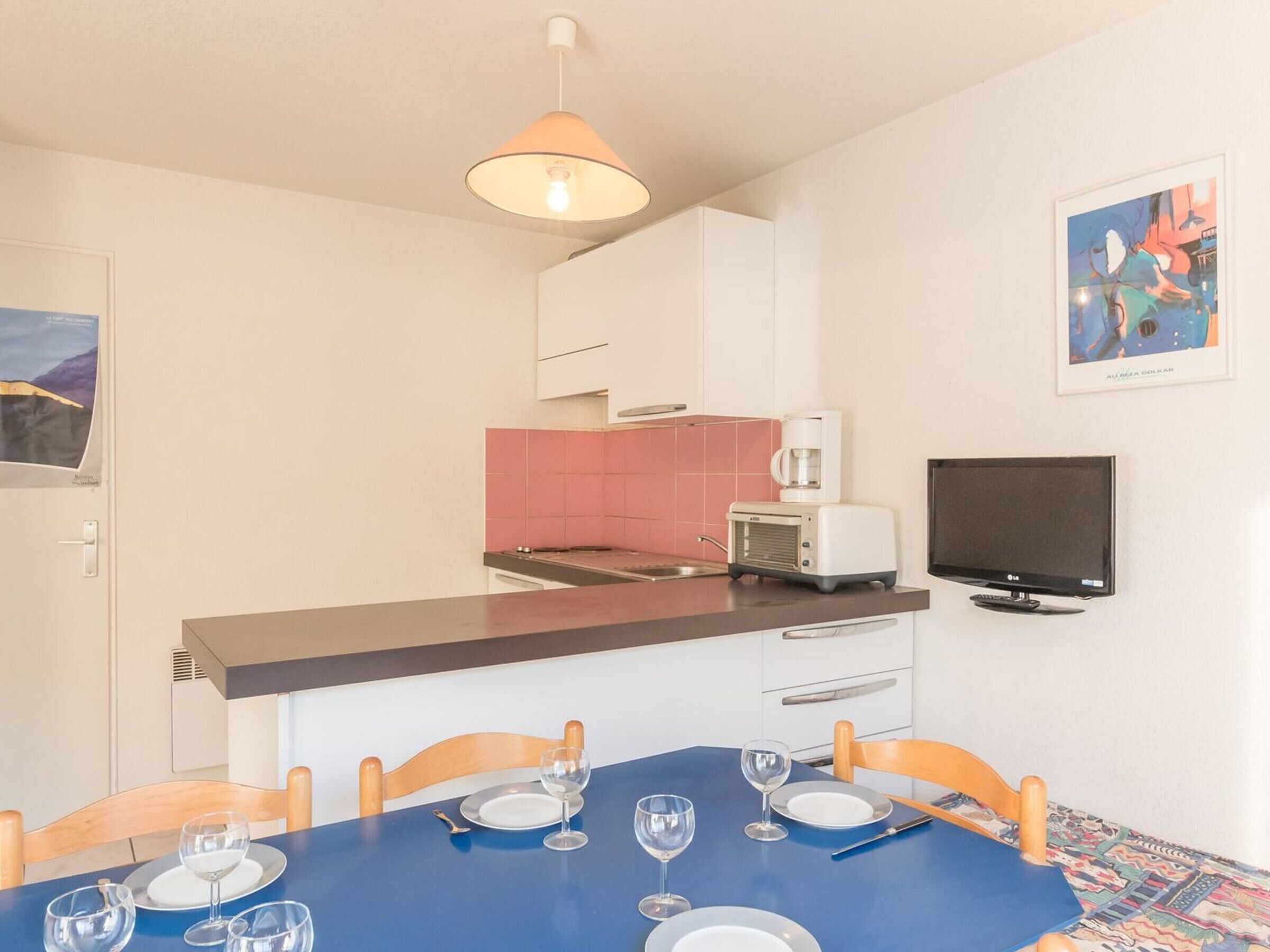 A compact kitchen with a microwave, toaster, and a flat-screen TV.