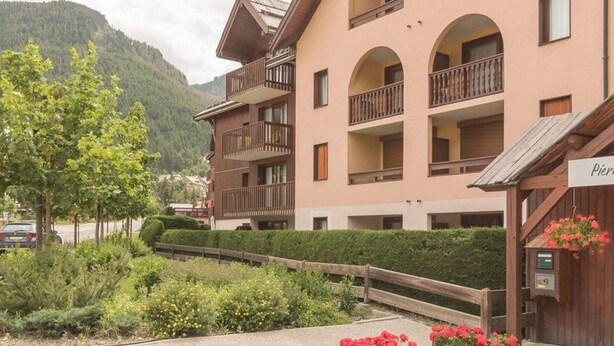 A multi-story hotel with balconies, surrounded by greenery and mountains.