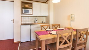 A compact kitchen with white cabinets, a microwave, and a coffee maker. There is a dining table with chairs and a hanging light fixture.