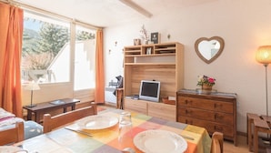 Un área de comedor con una mesa dispuesta para dos, un aparador de madera con estantes, un espejo con forma de corazón y una lámpara.