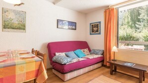 Una habitación acogedora con sofá, una mesa de comedor dispuesta con platos y vasos, y una ventana con cortinas.