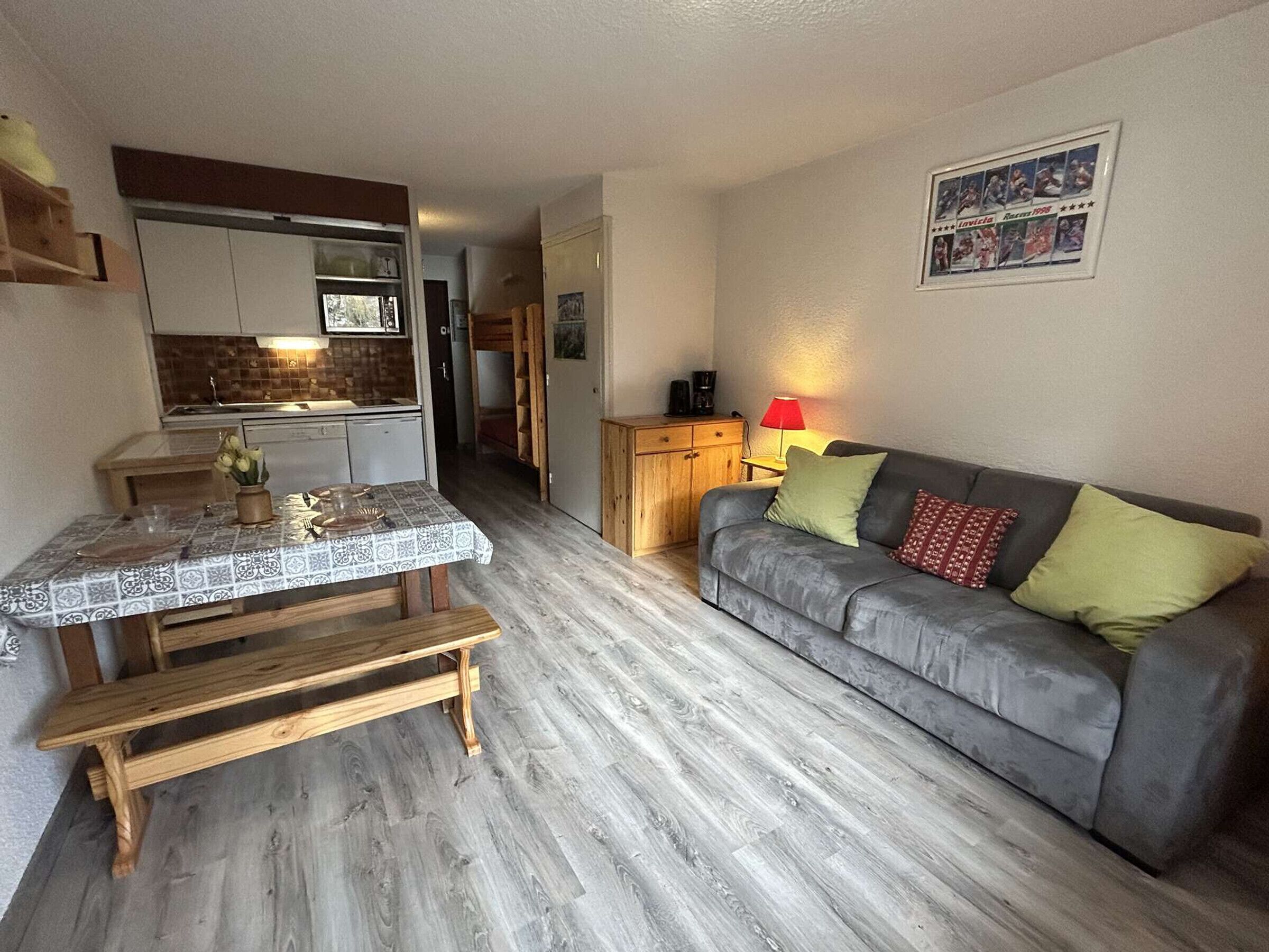 A compact living space with a kitchenette, a dining table, and a grey sofa with cushions.