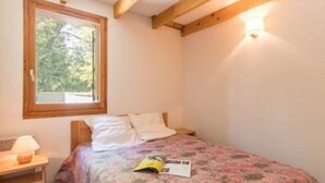 A bedroom with a bed, a nightstand, a window, and a wall-mounted light fixture.