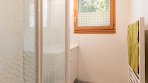 A bathroom with a glass shower enclosure, a wooden-framed window, and a towel hanging on a rack.