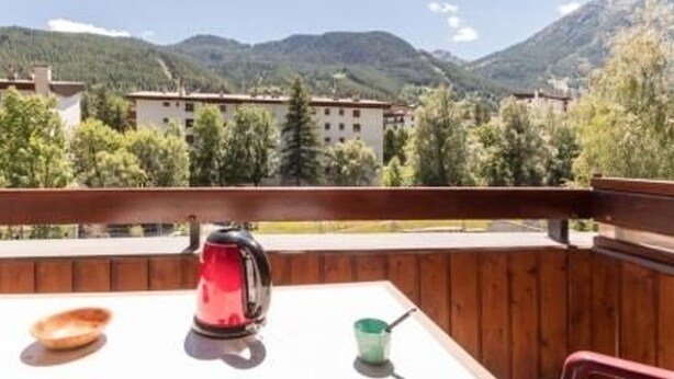 A balcony with a table, a red kettle, and a green cup.