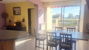 A dining area with a table and chairs, a television, and a door leading to an outdoor patio. - Carnon Centre. Very nice apartment 50 m2 +terrace 25m2, sea and garden view (Mauguio)