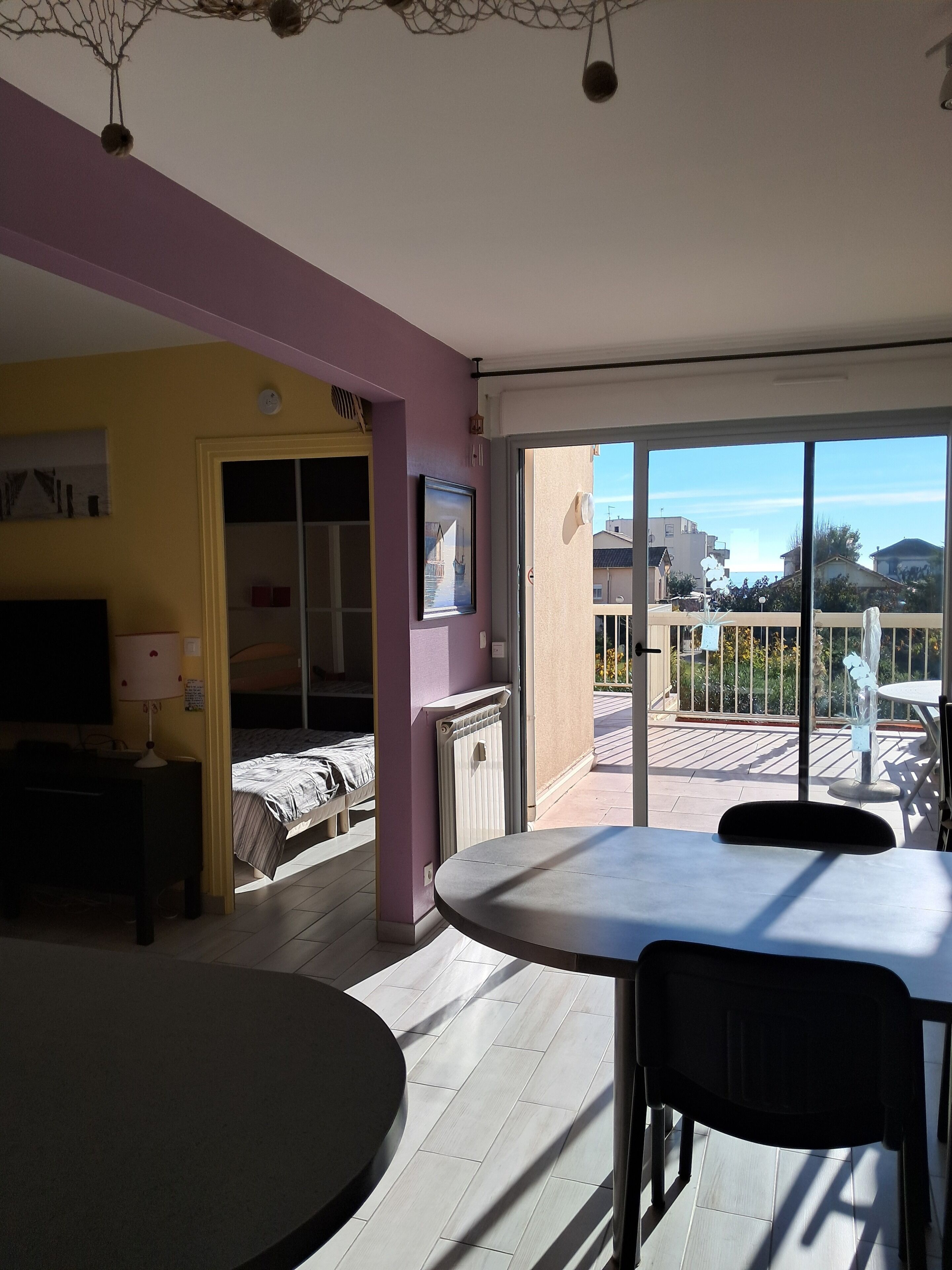 Ein Zimmer mit einem Bett, einem Tisch, einem Stuhl, einem Fernseher und einem Fenster mit Blick auf Gebäude und einem Balkon.