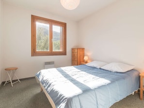 Quarto com cama, janela, mesa de cabeceira, abajur e uma pequena mesa.