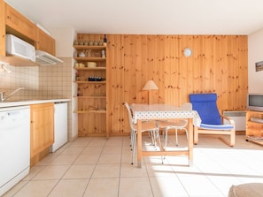 Cozinha compacta com armários de madeira, micro-ondas e  área de refeições com mesa e cadeiras.