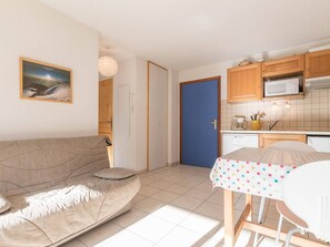 Uma sala de estar acolhedora com um sofá e uma mesinha, uma cozinha com armários de madeira e um micro-ondas, e uma porta azul.