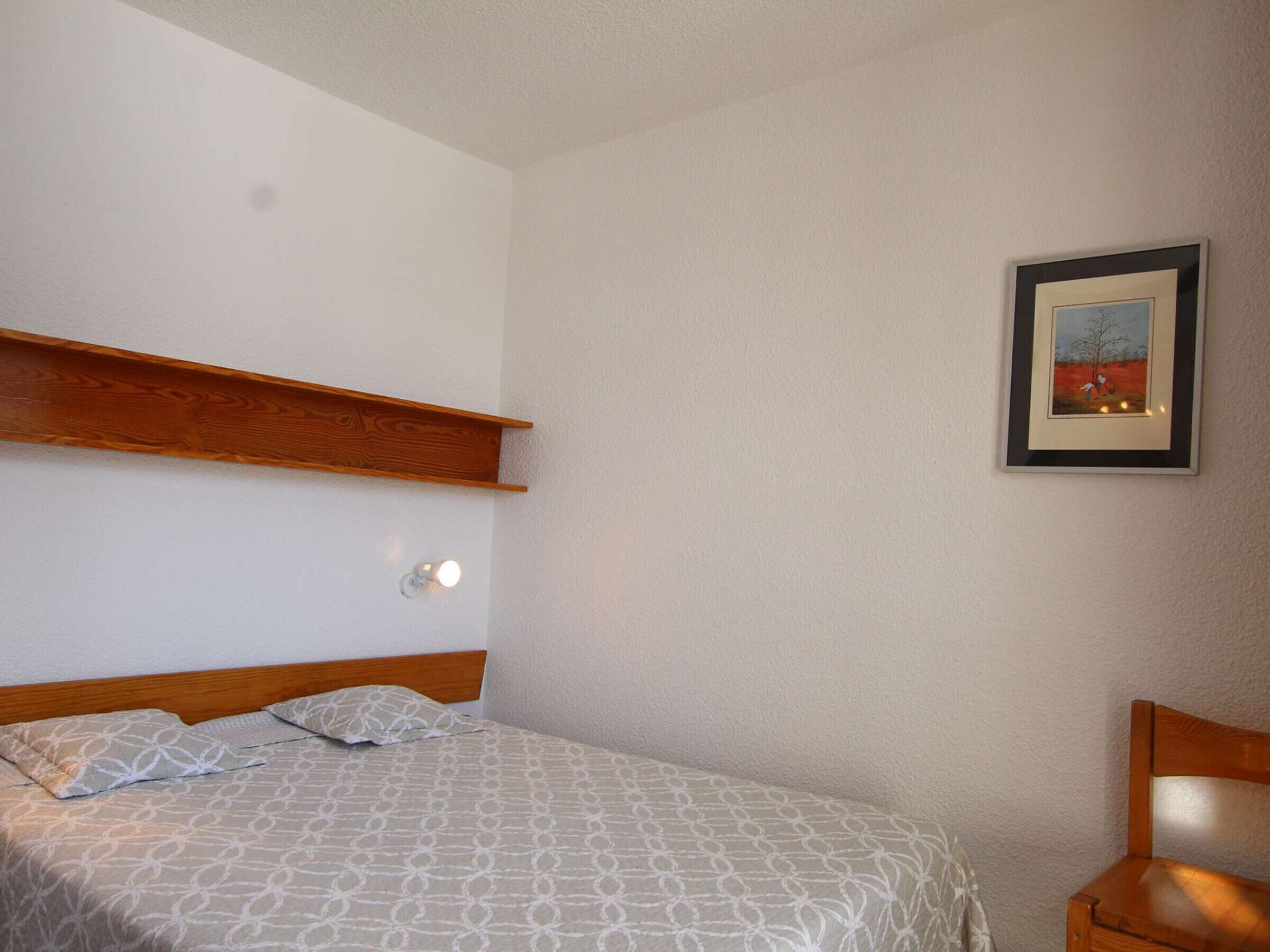 A bedroom with a bed, a wooden headboard, a nightstand, and a framed picture on the wall.