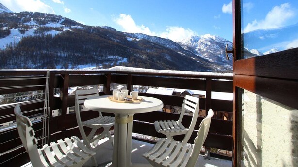 A balcony with a table and chairs, overlooking a snowy mountain landscape.