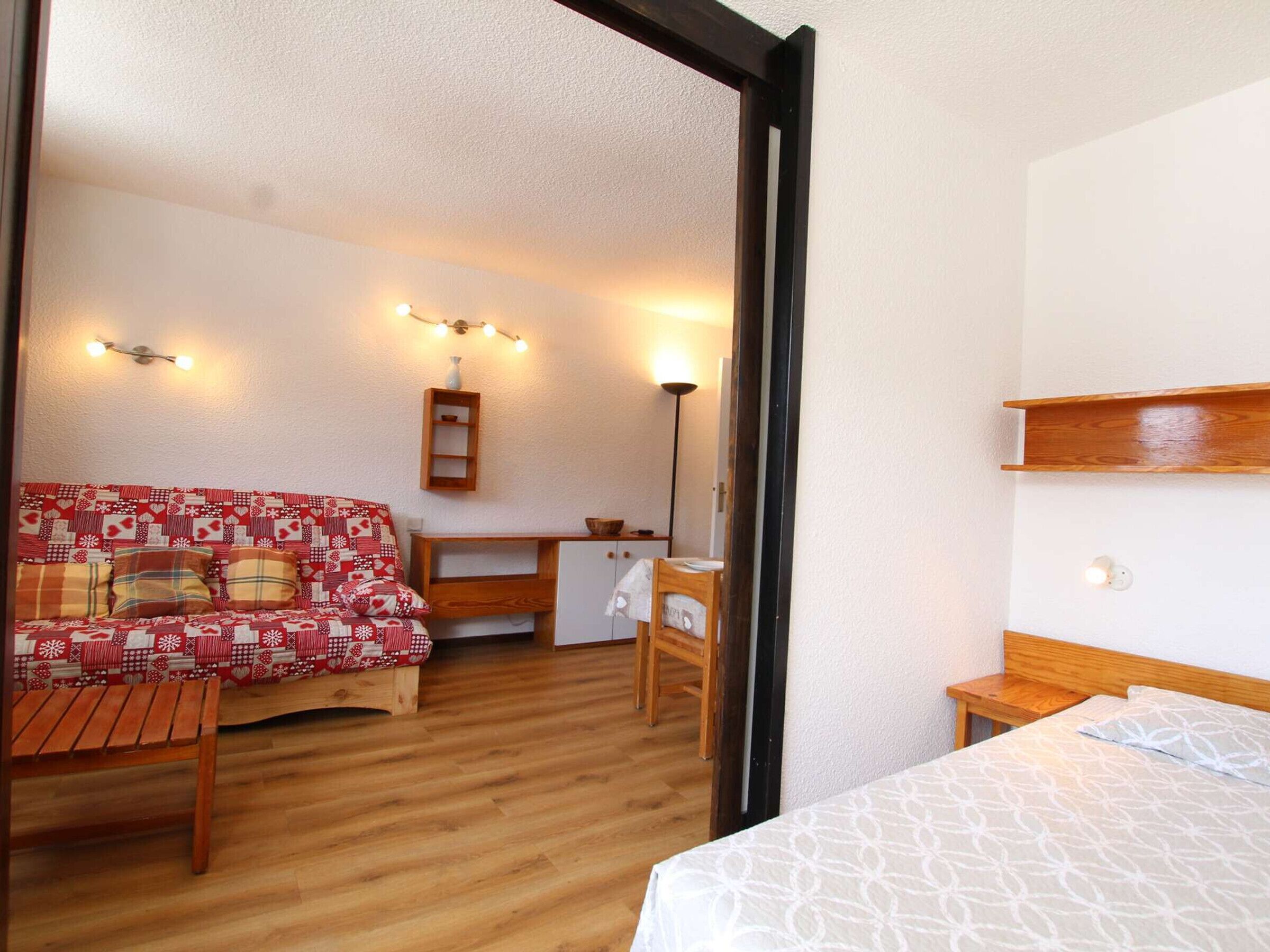 A cozy room with a wooden floor, a patterned sofa, a small desk, a chair, and a bed.