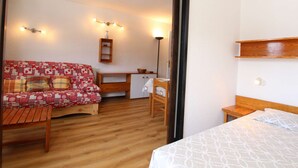 A cozy room with a wooden floor, a patterned sofa, a small desk, a chair, and a bed.