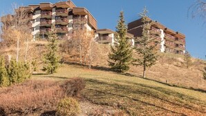 A multi-story hotel with balconies, set on a hillside with sparse trees and shrubs.