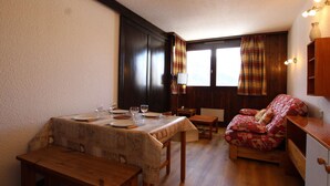 A cozy room with a wooden dining table set for four, a sofa with patterned cushions, and a small wooden cabinet.